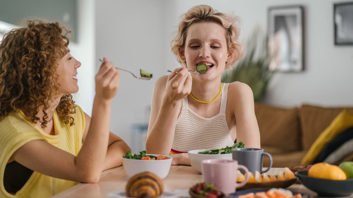 Two women enjoying a healthy meal at a cozy dining table, sharing a joyful indoor breakfast moment.